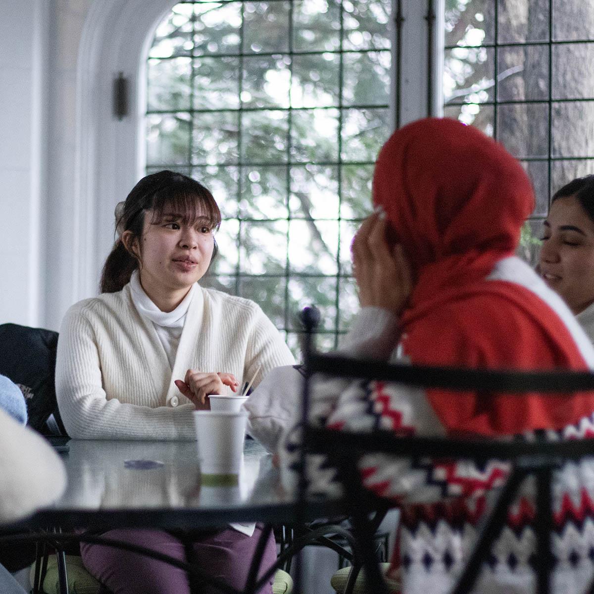 A group of international students sits at a table in Mellon, speaking together and smiling